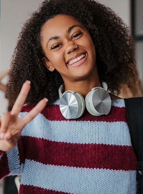 A student smiling and making a peace sign, wearing headphones around their neck.
